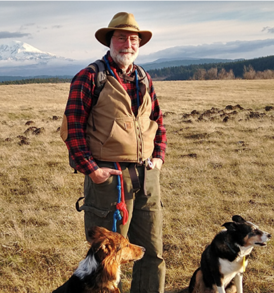 Picture of a man standing with his dog with plains and mountains in the background